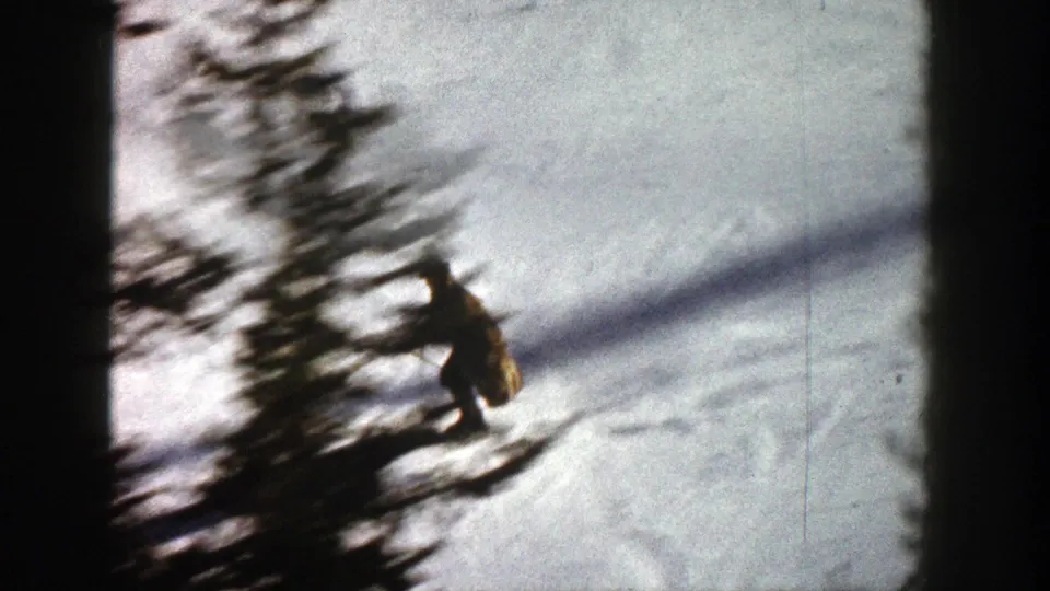 1961 Aspen 8mm frame with a distant skier passing near a blurred evergreen on a snowy slope.