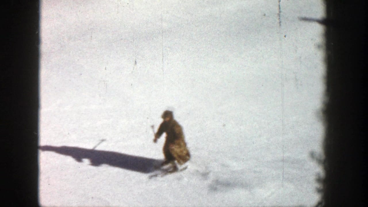 1961 Aspen frame of a skier using poles on a bright, open snowy slope with a long cast shadow.