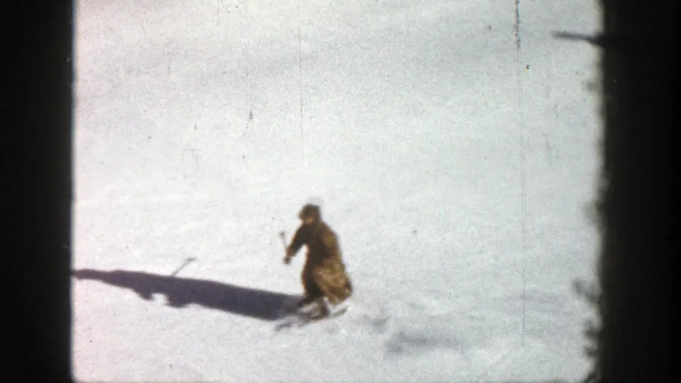1961 Aspen frame of a skier using poles on a bright, open snowy slope with a long cast shadow.