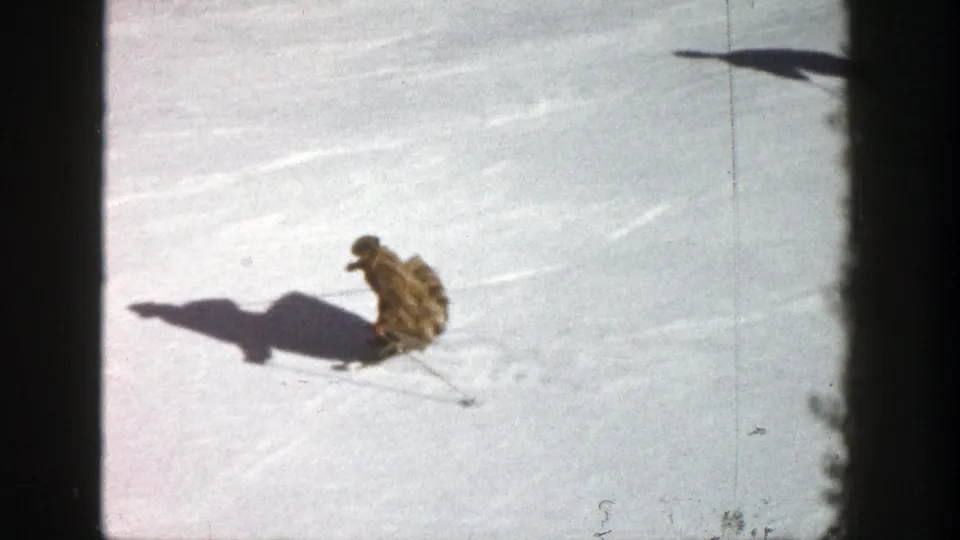 1961 Aspen home-movie frame showing a skier low to the snow during a turn or pause on the slope.
