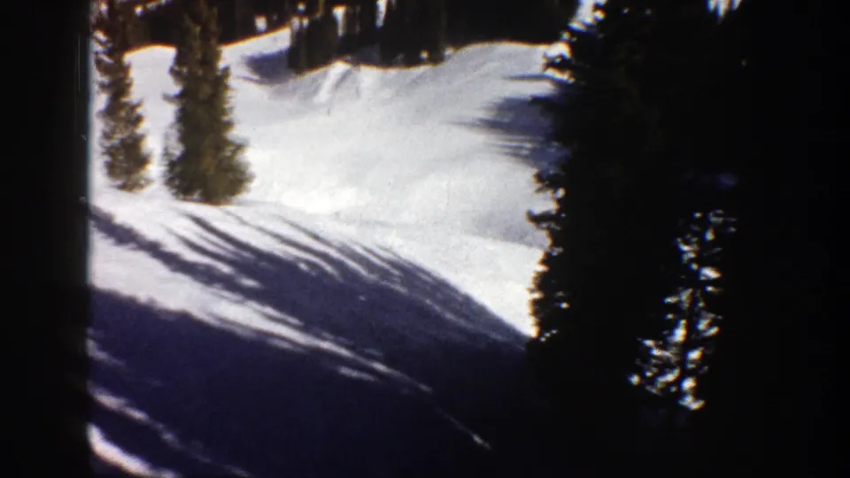 1961 Aspen home-movie frame showing evergreen trees and long shadows across a snowy mountain slope after the skiers pass.