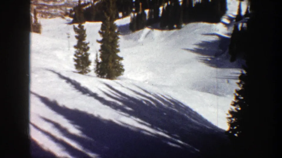 1961 Aspen home-movie frame showing a snow-covered slope bordered by evergreens and dark 8mm frame edges.