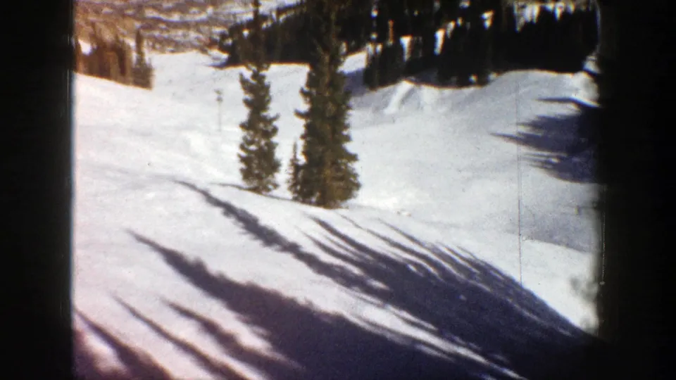 1961 Aspen 8mm frame showing a sunlit snowy slope with evergreen trees and long shadows across the snow.