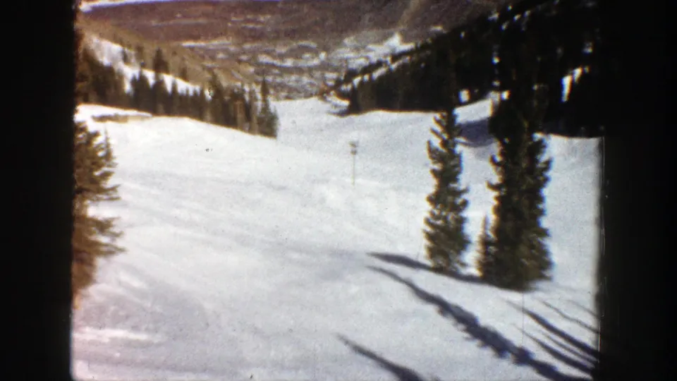 1961 Aspen winter frame showing two evergreens on a sunlit snow slope with distant terrain behind.
