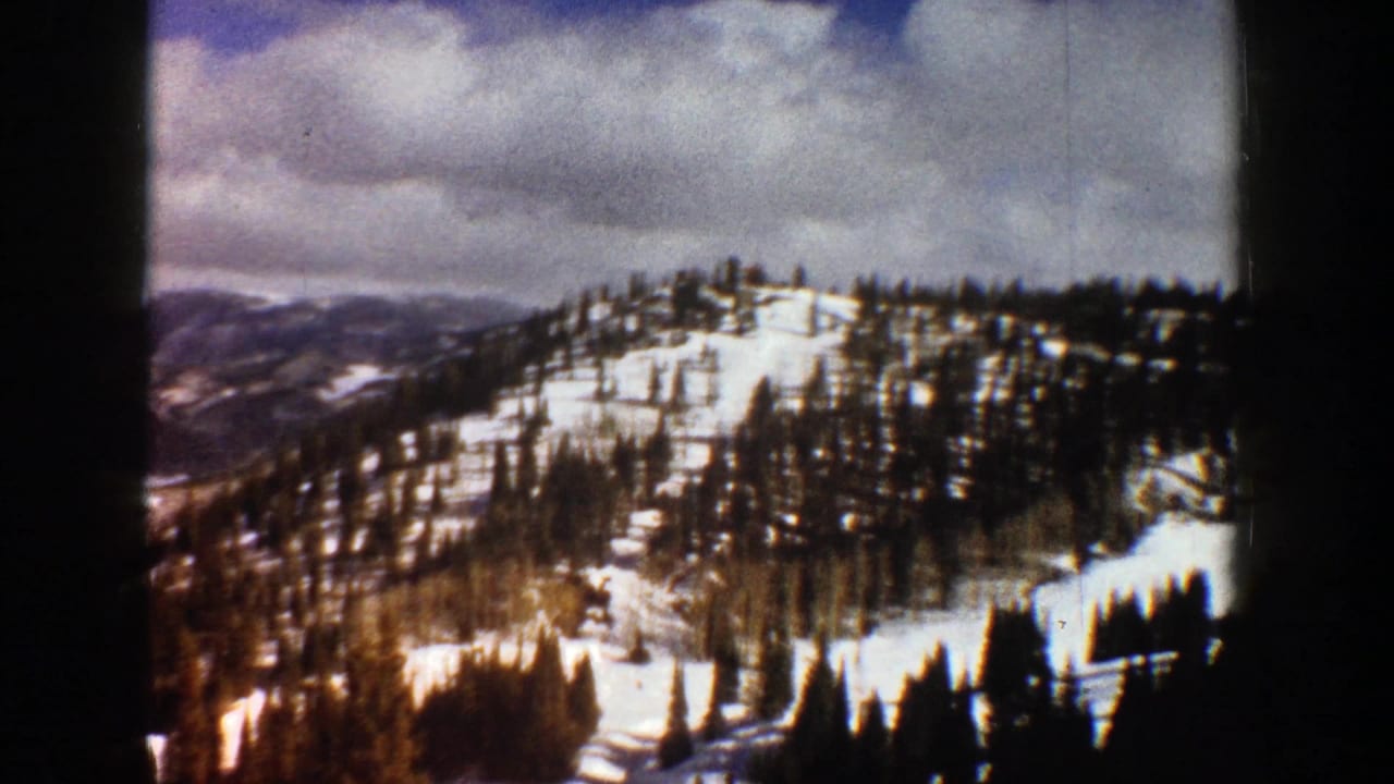 Snowy mountain ridge with pine trees under a partly cloudy sky.