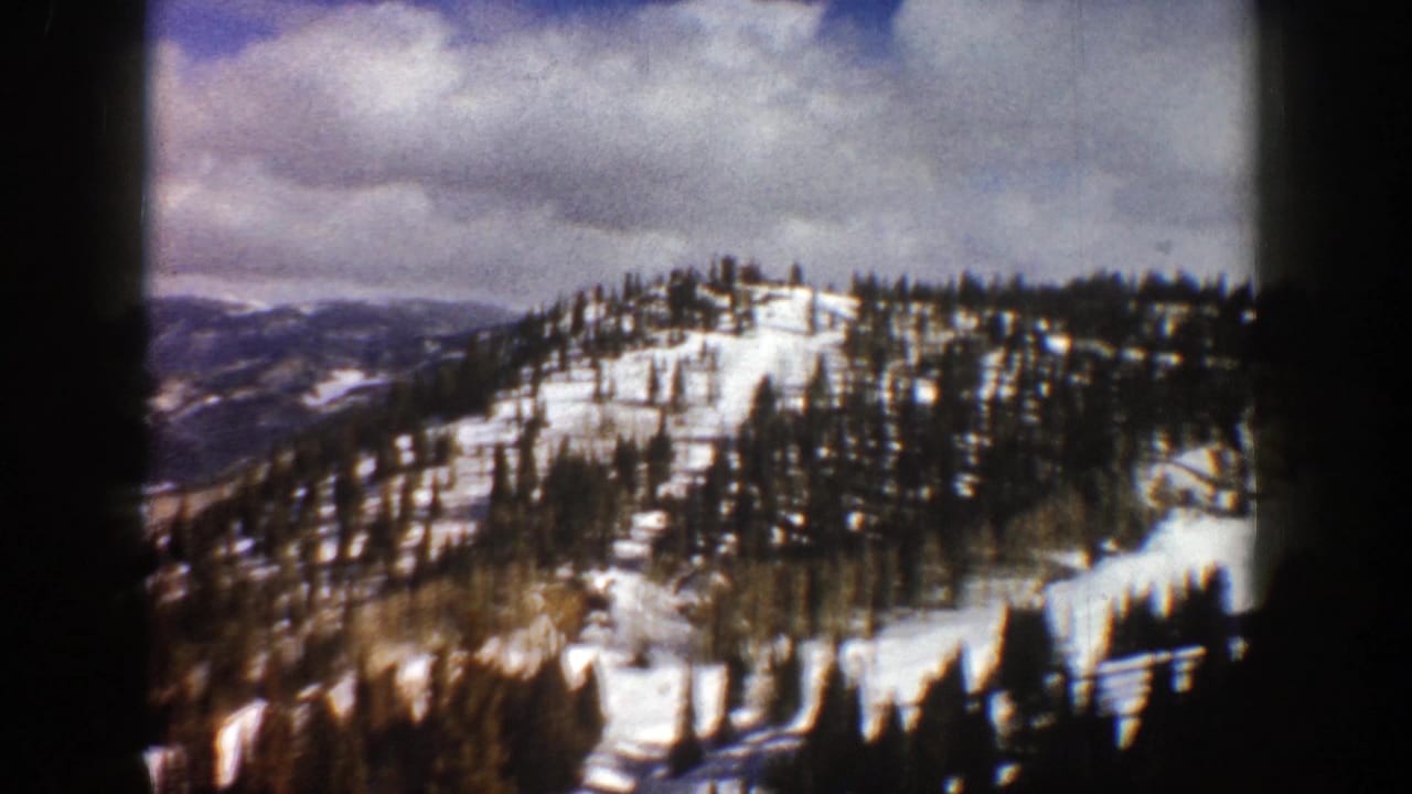 Snowy forested slope with distant ridgelines and cloud cover.