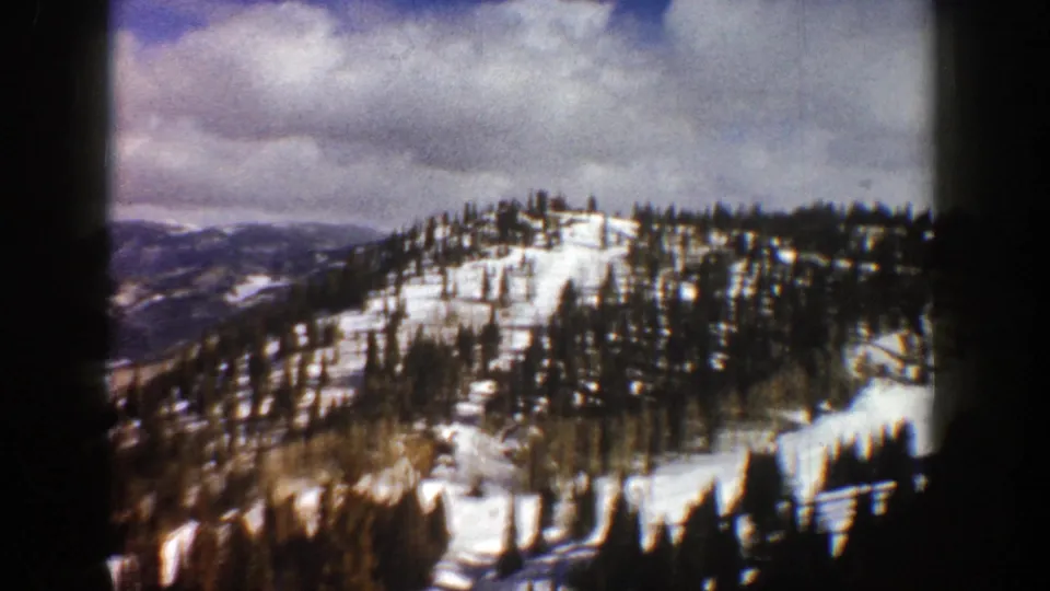 1961 Aspen, Colorado home-movie frame of a forested snowy slope, distant ridgelines, and heavy clouds within the 8mm gate.