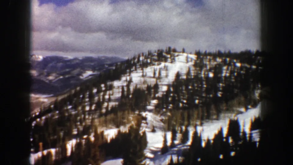 1961 Aspen, Colorado 8mm still showing a snowy hillside, scattered conifers, and muted mountain ranges in the distance.