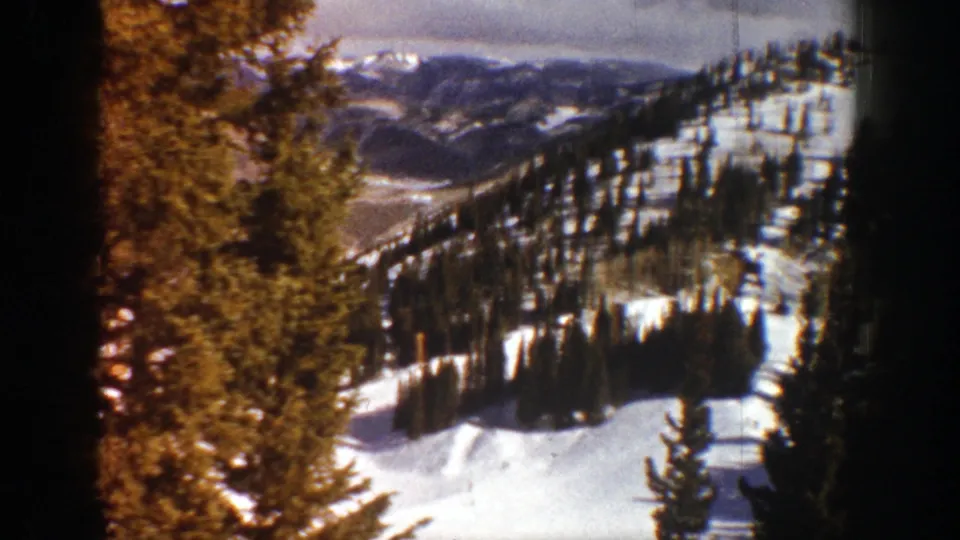 1961 Aspen, Colorado 8mm frame showing snow-covered mountain terrain, evergreens, distant ridgelines, and cloudy sky.
