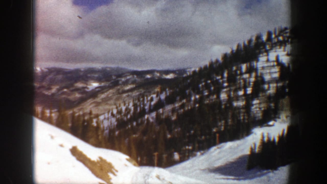 Snowy valley view with forested ridges and a cloudy mountain sky.