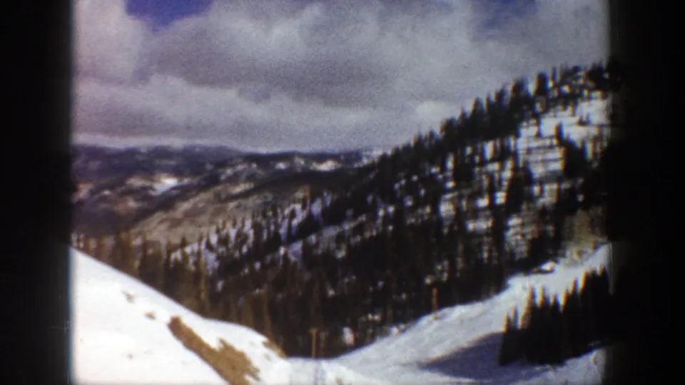 1961 Aspen, Colorado 8mm frame with a bright snowy slope in the foreground and darker evergreen-covered ridges beyond.