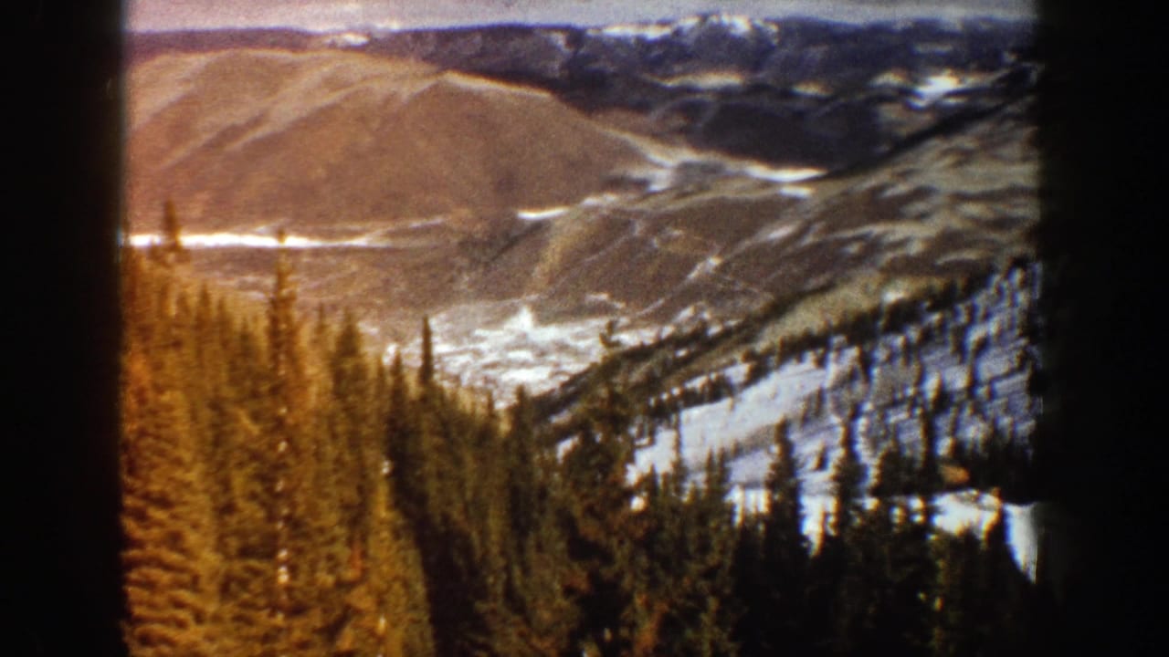 Snowy mountain valley with evergreen trees in the foreground and distant ridges beyond.