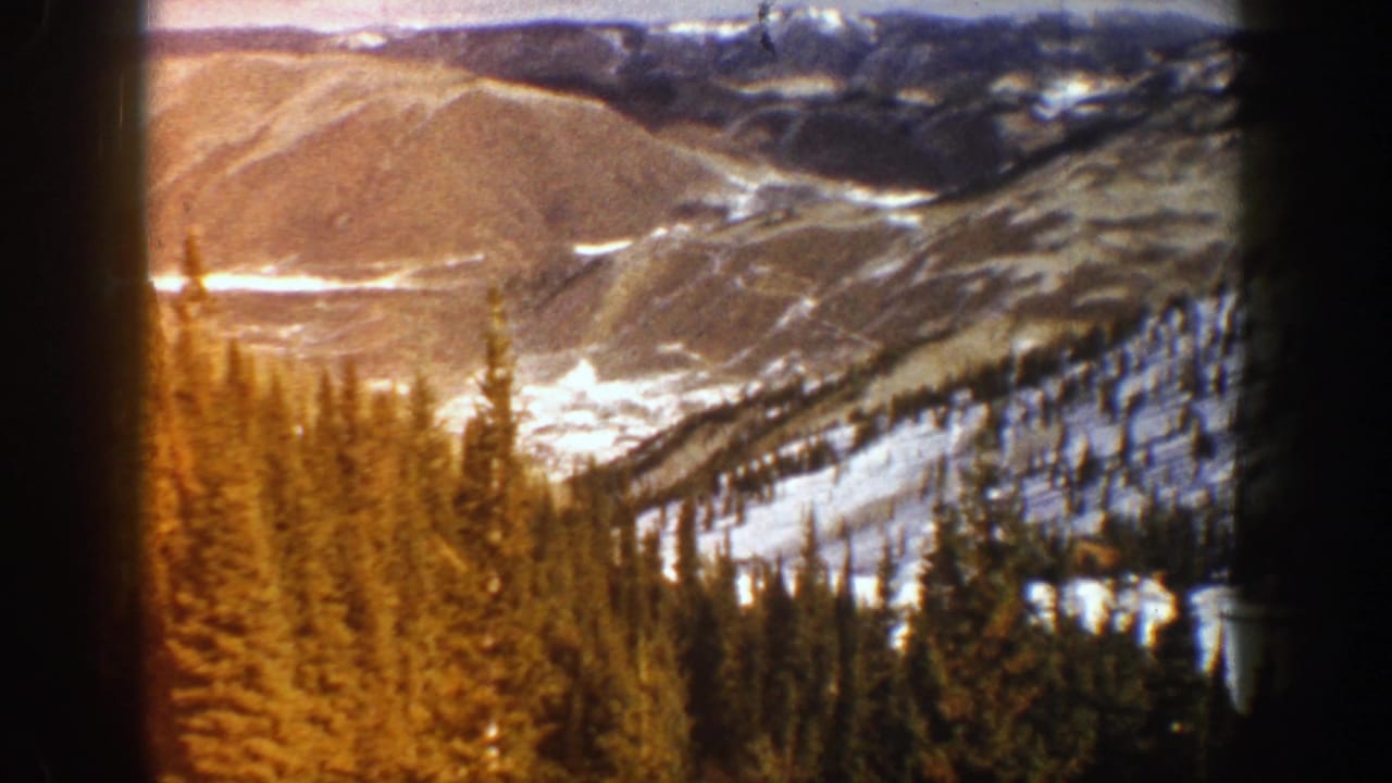 Warm-toned evergreen trees below snow-streaked hills and distant mountain ridges.