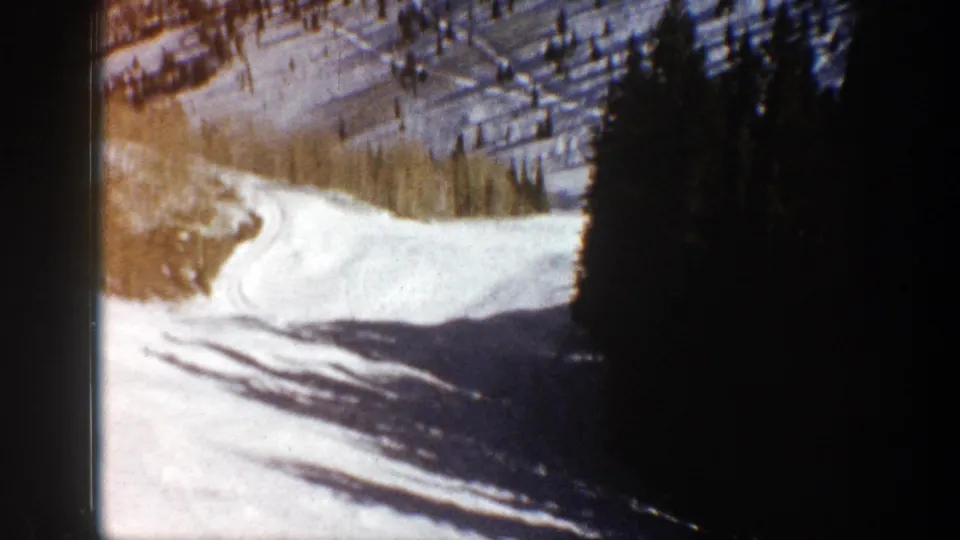 Aspen-area 8mm frame showing a closer snowy slope, scattered trees, long shadows, and a dark edge from the film frame.