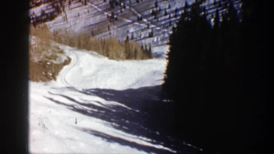 1961 Aspen home-movie frame showing a snow-covered slope descending past evergreens and pale aspen trees.