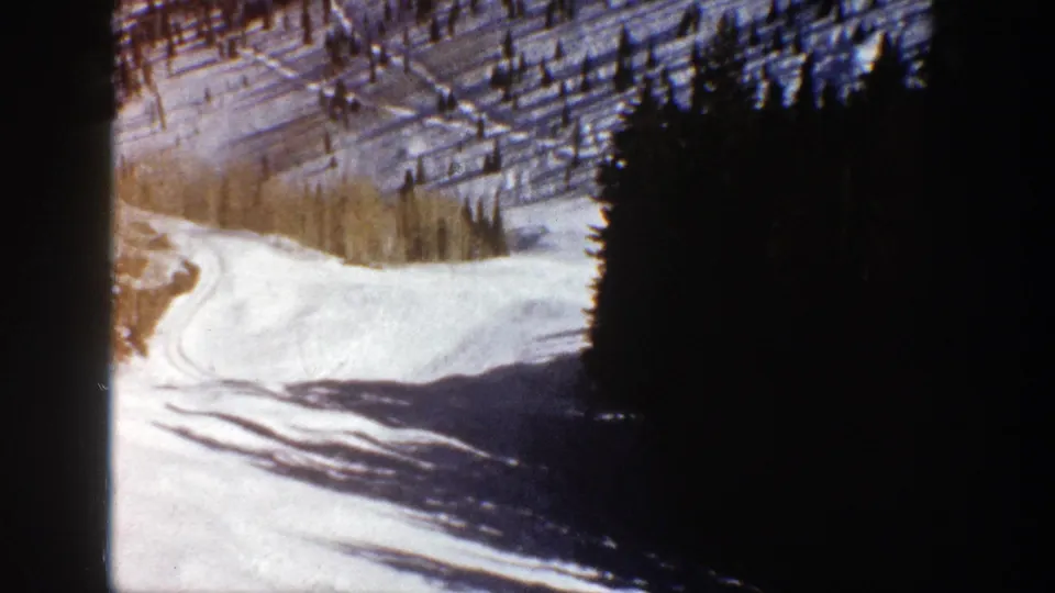 Aspen, Colorado 8mm frame with snow, curving tracks, dark evergreens, and pale trees in late-day light.