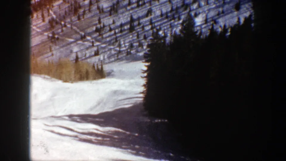1961 Aspen 8mm frame showing a snowy slope bordered by dense evergreens and pale trees in the distance.
