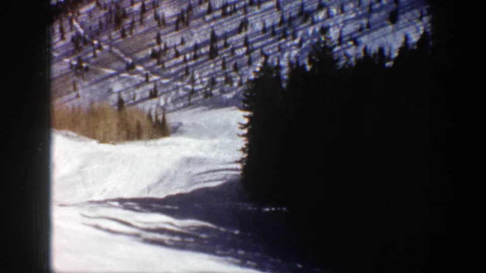 1961 Aspen-area 8mm frame showing a snow-covered slope, dark evergreen trees, and long shadows in bright sun.