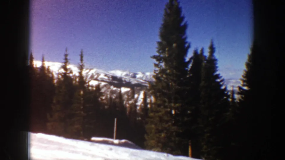 1961 Aspen-area 8mm frame with dark evergreens, a snow-covered foreground, and distant Rocky Mountain ridges.