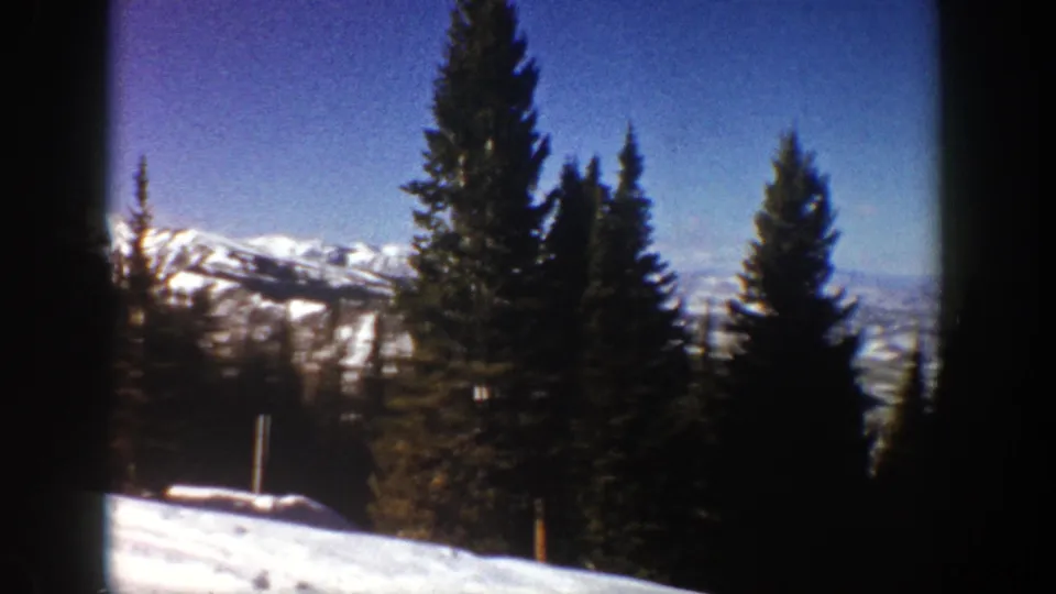 1961 Aspen-area winter landscape showing snow, clustered evergreens, distant ridges, and clear blue sky on 8mm film.