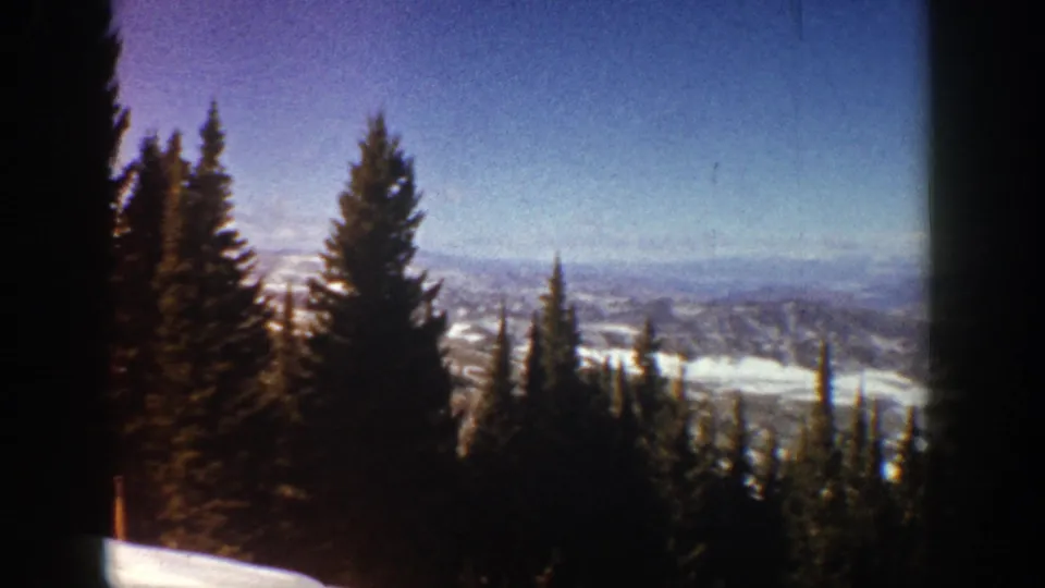 1961 Aspen, Colorado 8mm frame showing a winter overlook through tall pines toward a hazy mountain valley.