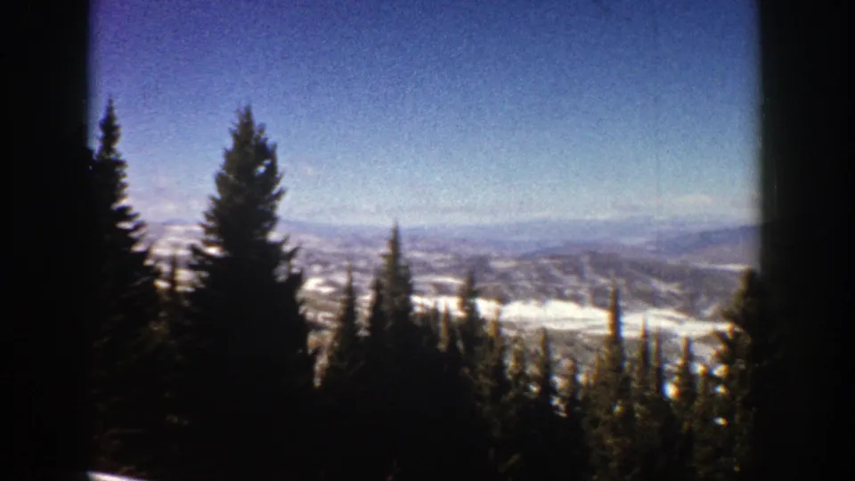 1961 Aspen, Colorado home-movie frame with pines at the edge of a snowy overlook and distant winter terrain.