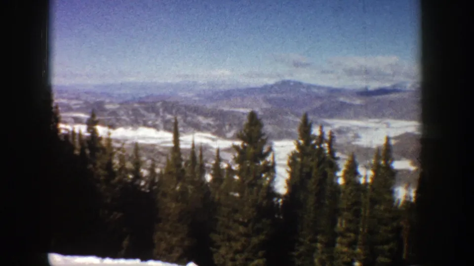 1961 Aspen, Colorado 8mm frame with evergreen treetops in the foreground and snowfields across distant ridges.