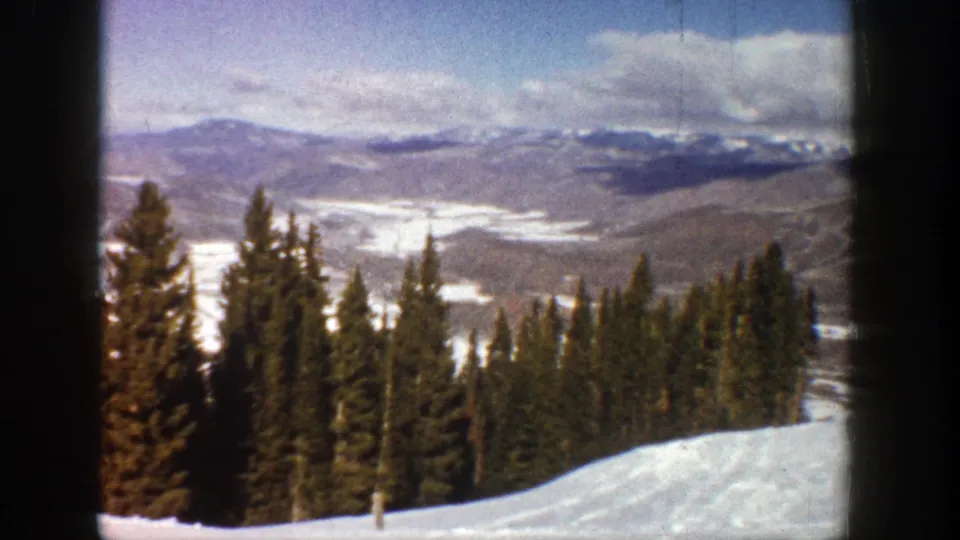 8mm winter view near Aspen with pine trees, a white slope, and distant Colorado mountain terrain.