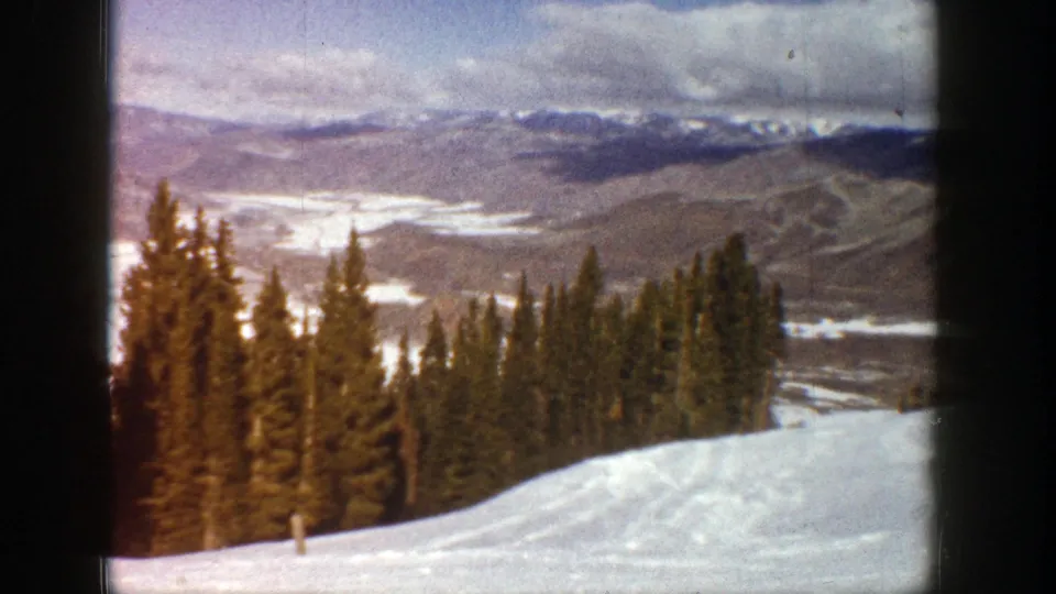 Vintage 8mm frame from Aspen showing a winter overlook with evergreens, snow, and distant ridgelines.