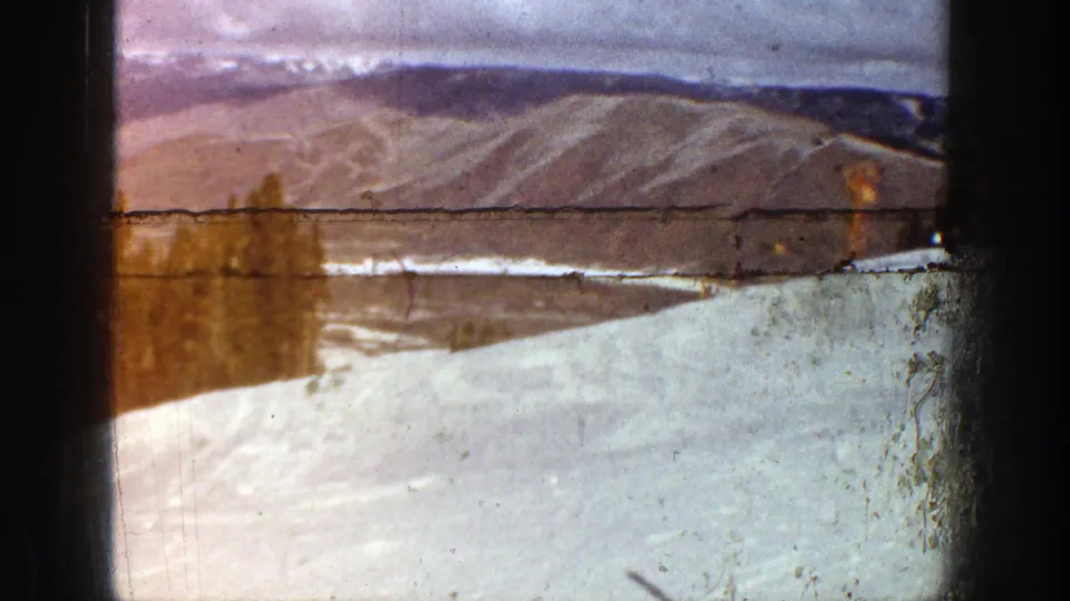 Home-movie view of Aspen snow and distant mountain ridges, with a horizontal film mark and visible wear from the 8mm source.
