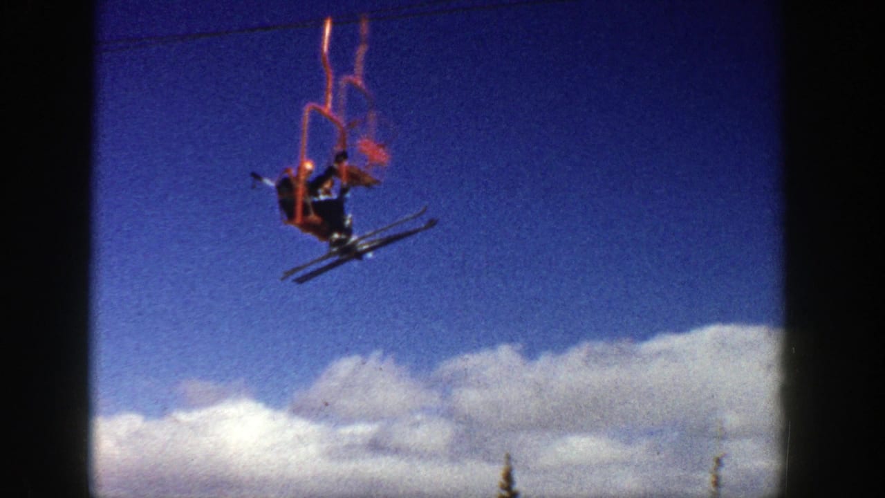 A skier rides a red chairlift with skis hanging below against blue sky and clouds in Aspen, Colorado, according to the 1961 clip metadata.