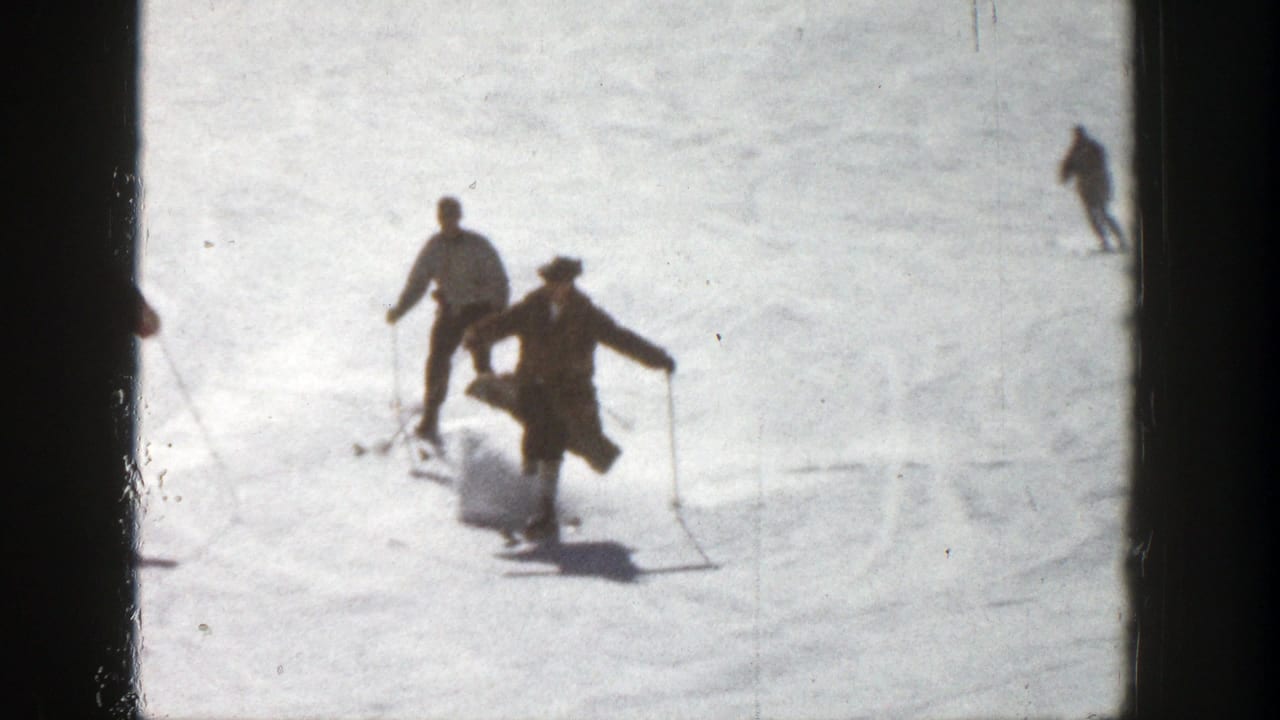 Two skiers descend a bright snowy slope while another skier appears farther back.