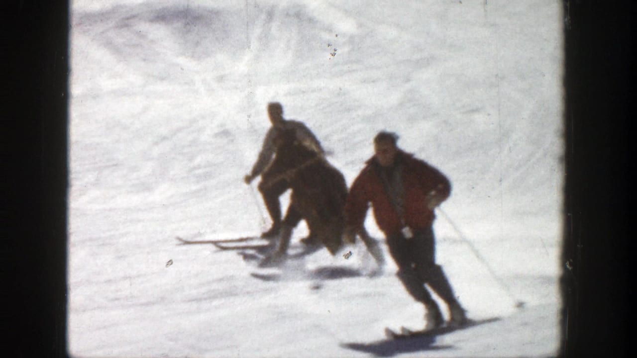 Skiers in winter clothing pass across the snowy Aspen slope, with one red jacket standing out against the bright snow.