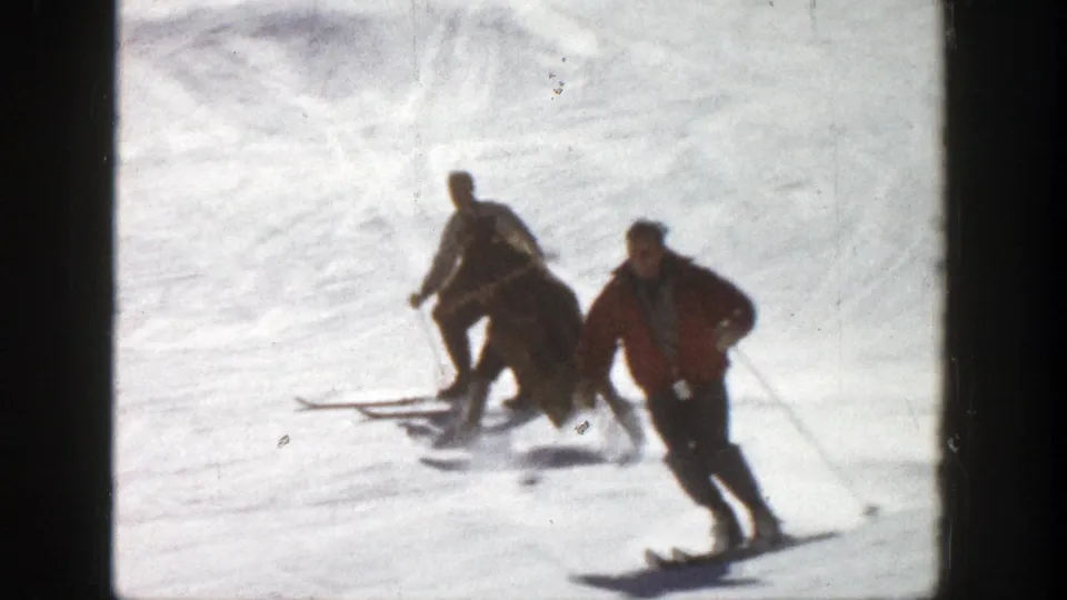 Skiers in winter clothing pass across the snowy Aspen slope, with one red jacket standing out against the bright snow.