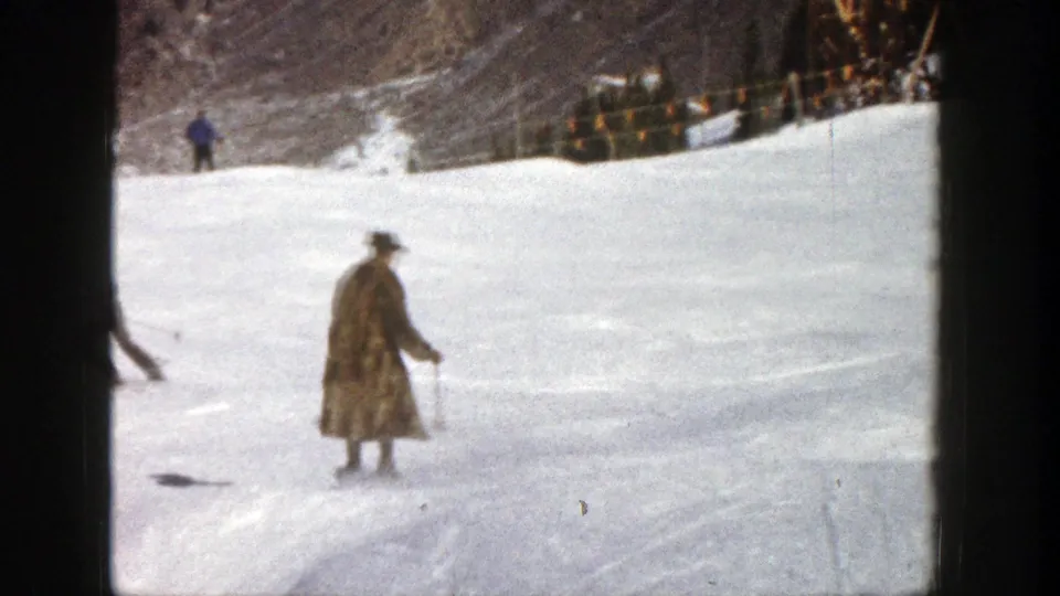 Rear view of a fur-coated skier on an Aspen snow slope in 1961, filmed in soft 8mm color with distant skiers nearby.