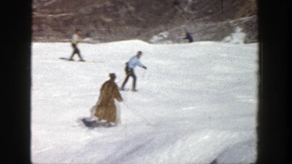 1961 Aspen home-movie still showing a fur-coated skier descending while other skiers traverse the open snowfield.