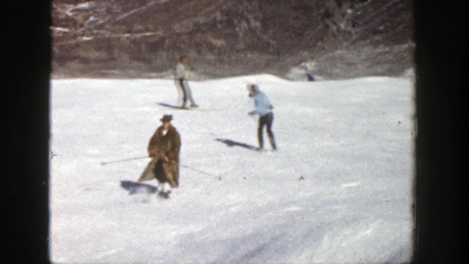 1961 Aspen, Colorado home-movie frame showing a man in a brown fur coat skiing backward while other adults ski behind him.