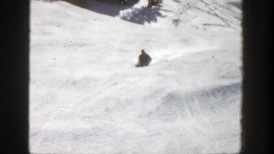 1961 Aspen frame showing a skier low on the snow, possibly seated or sliding, on a beginner slope.