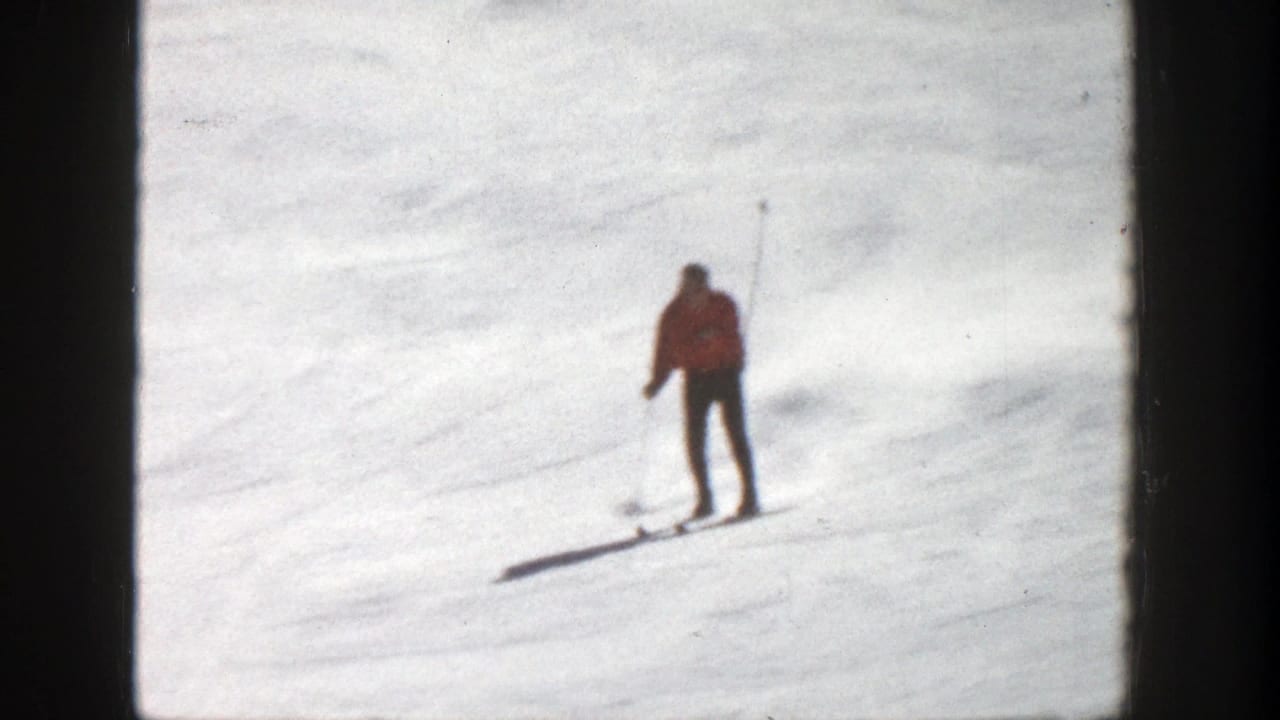 A skier in a red jacket moves downhill on a snowy Aspen slope in 1961 home-movie footage, framed by dark 8mm borders.