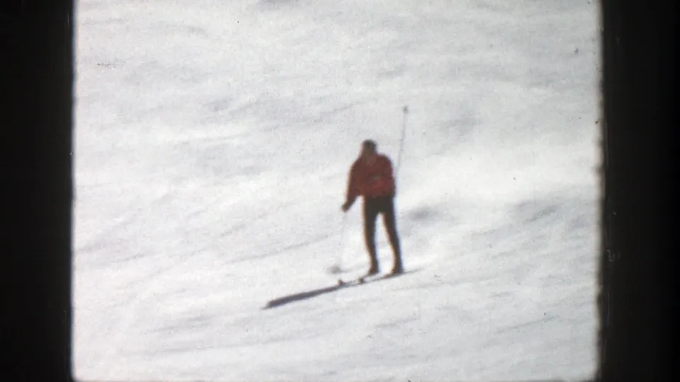 A skier in a red jacket moves downhill on a snowy Aspen slope in 1961 home-movie footage, framed by dark 8mm borders.