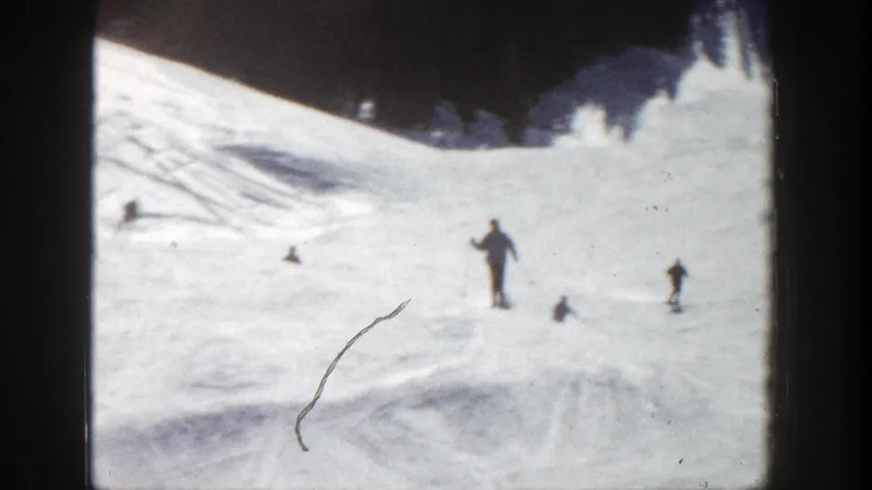 Several skiers are spread across an Aspen snow slope, with visible ski tracks, dark borders, and a scratch in the 8mm frame.