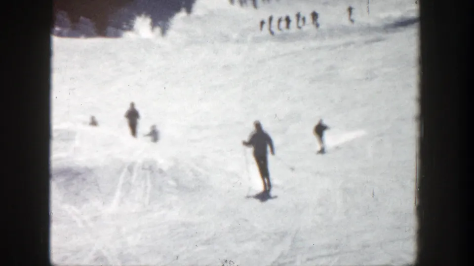 1961 Aspen home-movie frame showing scattered skiers in dark winter clothing on a snowy slope.