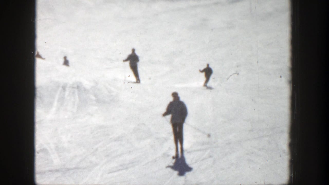 A skier with poles stands or glides in the foreground while others ski farther uphill.
