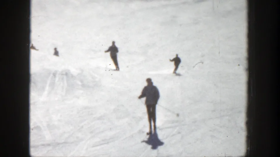 1961 Aspen 8mm frame with a foreground skier using poles and several distant skiers on the snow.