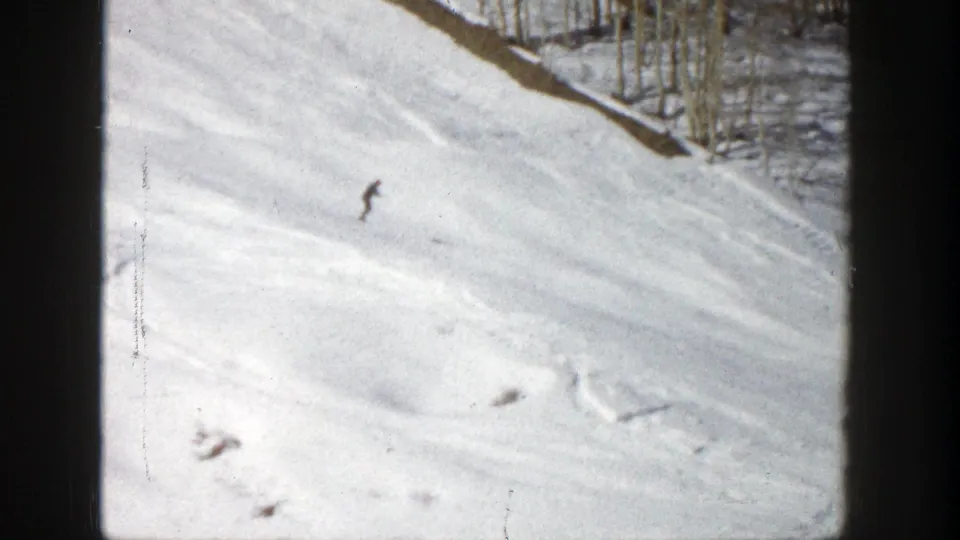 1961 Aspen home-movie frame showing a distant skier on a wide snowy run beside trees.