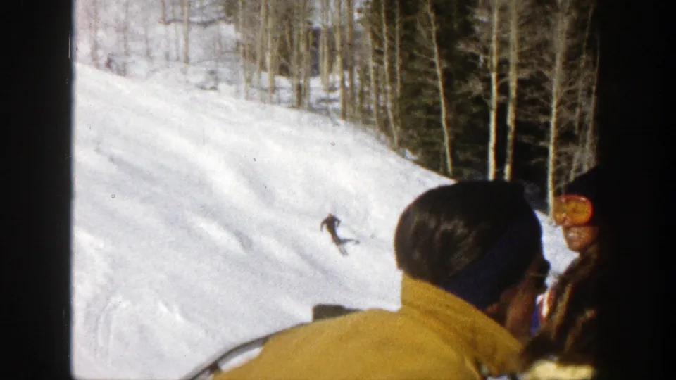 People on a ski lift, including a person in a yellow sweater, look toward a skier descending an Aspen slope in 1961.