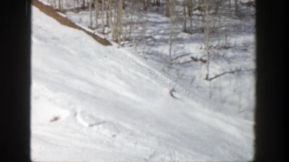 A distant skier carves across a snowy wooded Aspen slope in 1961, seen through an 8mm home-movie frame.