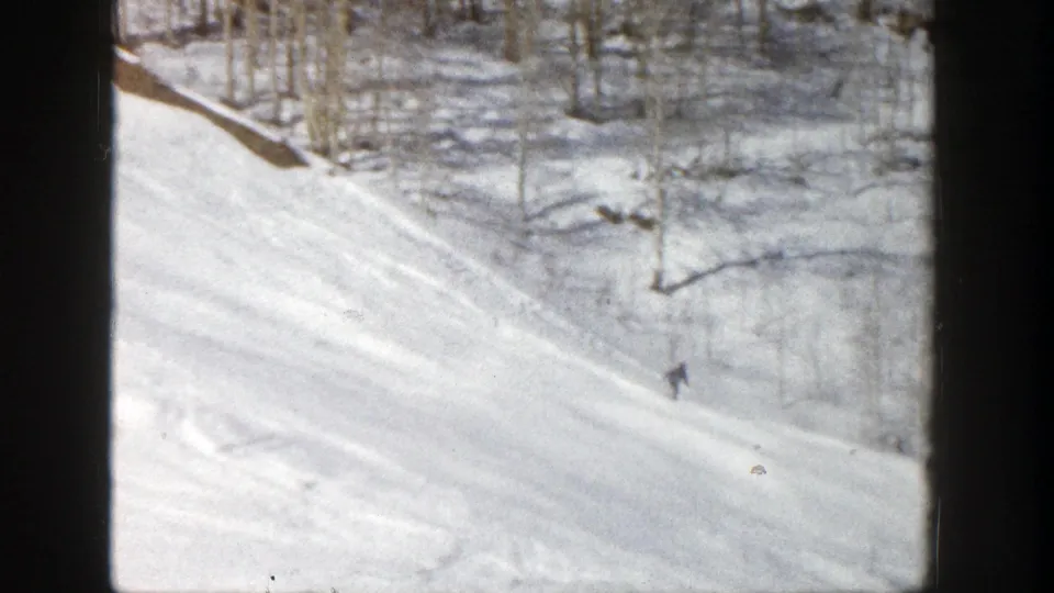 1961 Aspen ski slope viewed from behind dark supports, with small skiers descending through snowy trees.