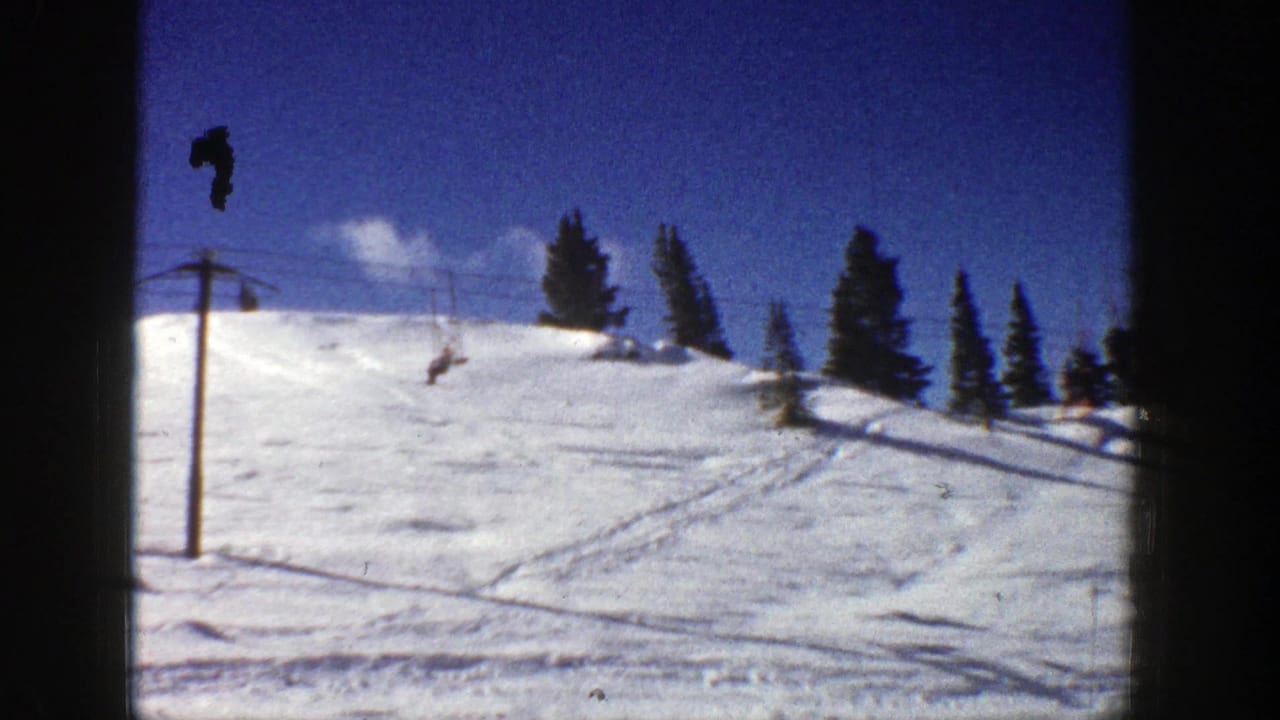 Chairlift tower and cable with riders above a tracked snowy hillside.