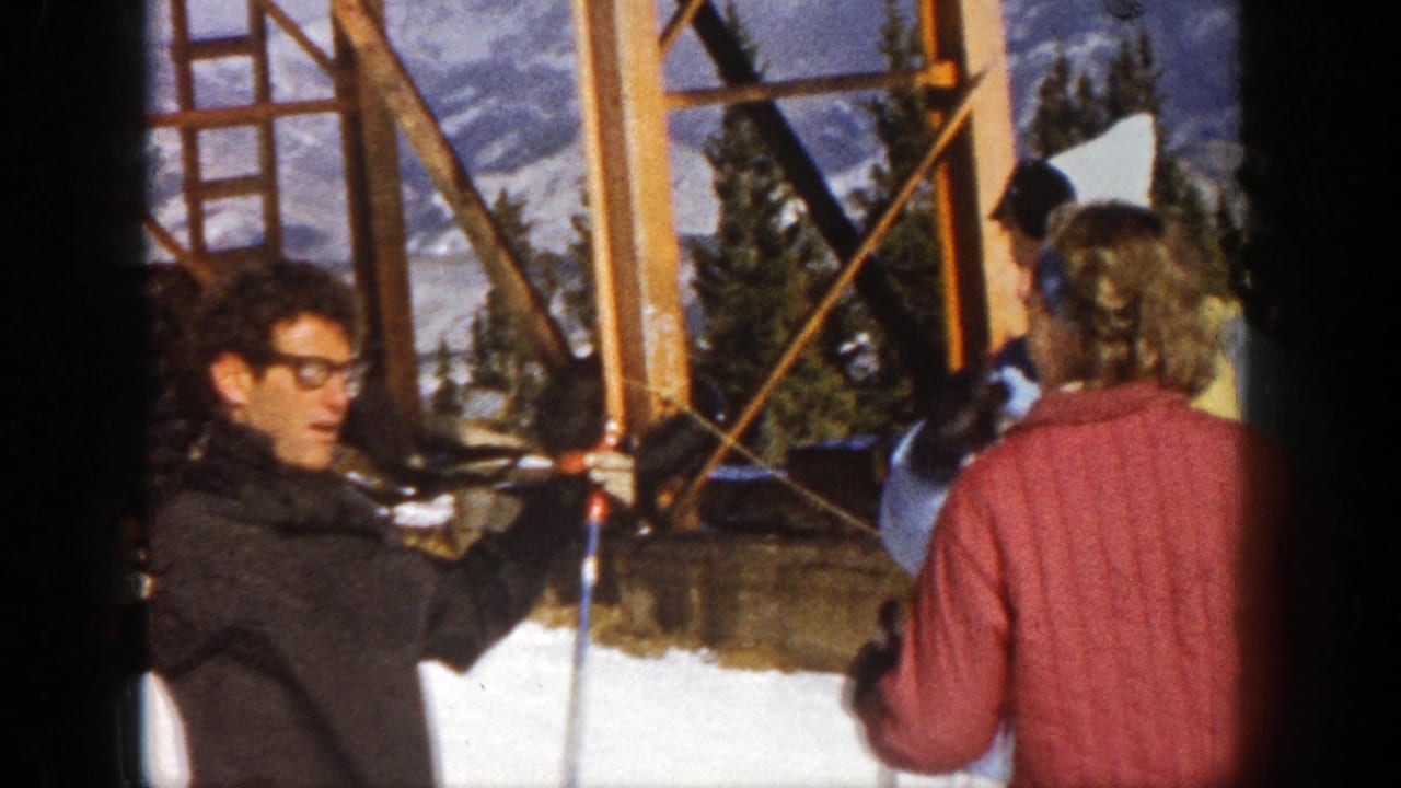 Skiers stand near a wooden lift structure while a man holds ski poles.